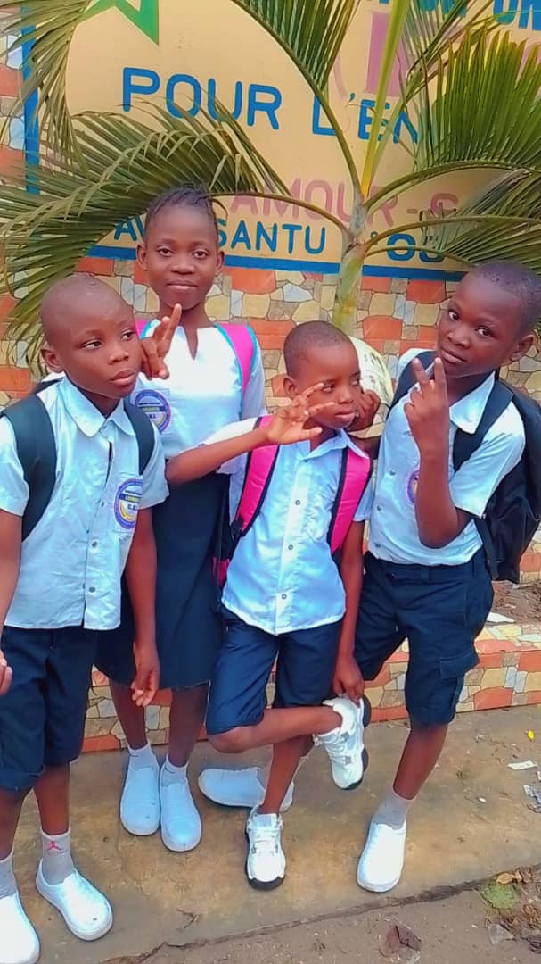Quatre enfants en uniforme scolaire devant la pancarte de la fondation
