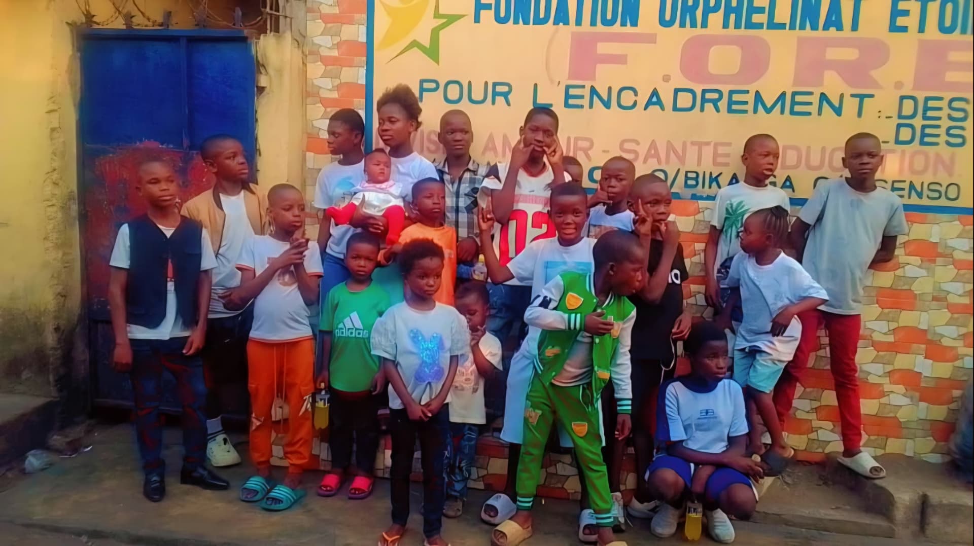 Groupe d'enfants de la fondation réunis devant la pancarte de l'orphelinat Étoile Brillante